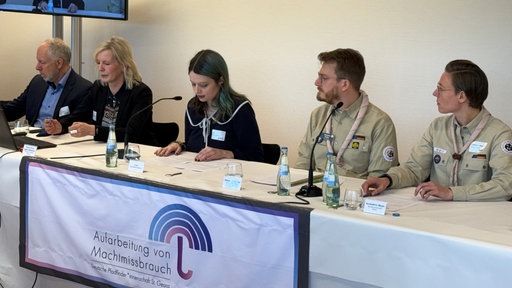 Auf dem Bild sieht man eine Pressekonferenz der Mönchengladbacher Pfadfinder. Insgesamt sitzen fünf Personen an einem Tisch. 