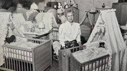 Eine Verkäuferin steht zwischen Baby-Wiegen, das Foto ist schwarz-weiß