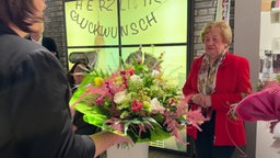 Eine Frau in einem roten Blazer bekommt einen Blumenstrauß überreicht
