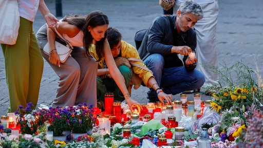 Auf dieser Aufnahme aus dem August 2024 ist zu sehen, wie mehrere Menschen knien und Kerzen abstellen