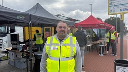 Rainer Geiser mit Gelber Warnweste steht vor roten verdi Zelten.