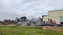 Eine abgebrannte Halle einer Abfallsortierungsanlage. Links daneben ein Löschfahrzeug.