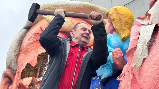 Der Düsseldorfer Wagenbauer Jacques Tilly schlägt mit einem Hammer auf ein konstruiertes Gesicht seiner Karnevalswagen ein.