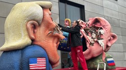 Der Düsseldorfer Wagenbauer Jacques Tilly reißt Stücke aus einer Figur des Gesichts Donald Trumps, gegenüber dieses Gesichts ist Wladimir Putin.