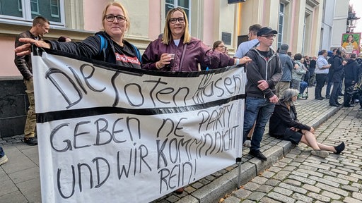 Anja und Susanne halten Banner zum Toten-Hosen-Konzert in Düsseldorf hoch. Darauf steht Die Toten Hosen geben ne Party und wir kommn nicht rein