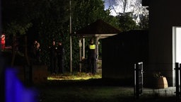 Mehrere Polizisten stehen im Dunkeln in einem Garten und unterhalten sich.