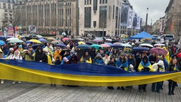 Die Demonstrierenden halten ein langes Banner in den Farben der ukrainischen Flagge