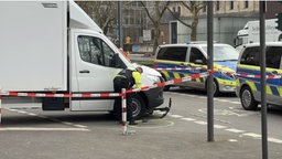 Zu sehen ist der Unfallort, bei welchem unter einem weißem LKW ein E-Scooter liegt.