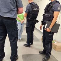 Drei Zollbeamte stehen bei einer Zivilistin