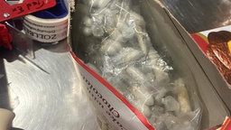 eine offene Keksschachtel, worin Kapseln mit Vogelspinnen enthalten sind 