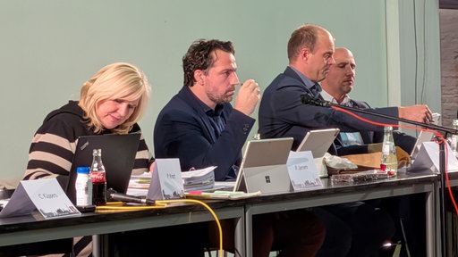 Drei Männer und eine Frau sitzen an einem Tisch