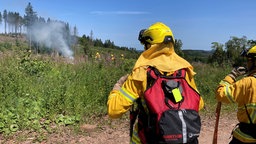 Zu sehen sind zwei Feuerwehrleute auf der Waldfläche.