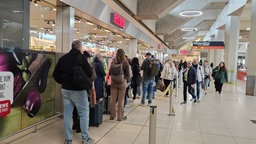 Menschen stehen im Flughafen Köln/Bonn vor einem Supermarkt