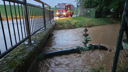 Ein Rohr ragt aus einem überfluteten Behältnis raus. Im Hintergund steht ein Feuerwehrauto 