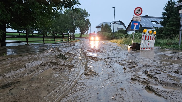 Eine mit Matsch bedeckte Straße, im Hintergrund nähert sich ein Auto.