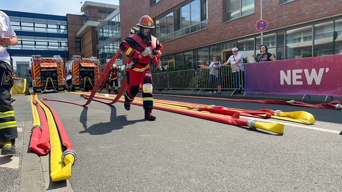 Ein Feuerwehrmann zieht zwei Schläuche, die auf seinen Schultern liegen
