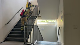 Zwei Feuerwehrfrauen in voller Ausrüstung rennen ein Treppenhaus hoch