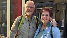 Ein Mann und eine Frau stehen Arm in Arm in der offenen Tür eines Regionalzugs und lächeln in die Kamera.