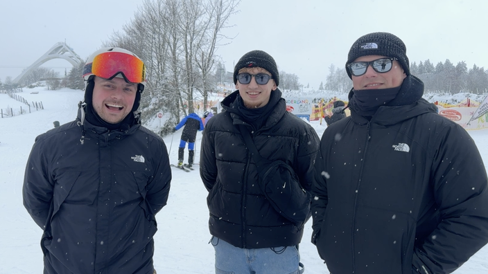 3 lächelnde Männer in Winterkleidung auf der Ski-piste