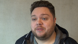 Ein junger Mann mit Kapuzenpullover steht vor einer grauen Wand