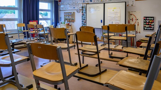 Leerer Klassenraum, Stühle stehen auf dem Tisch, im Hintergrund eine weiße Tafel