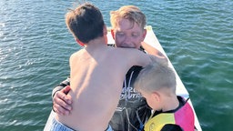 Ein Mann nimmt zwei Kinder auf einem Wakeboard in den Arm
