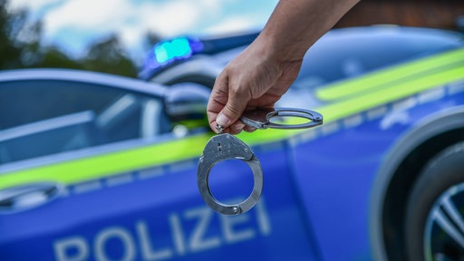 Das Foto zeigt Handschellen vor einem Polizeiauto