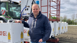 Landwirt Carsten Abenhardt steht neben seinem Traktor auf einem Feld. Sein Arm liegt auf einem der Roboter-Module am Heck des Fahrzeugs. 
