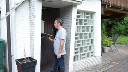 Ein Mann steht vor seiner Haustür und öffnet den leeren Briefkasten.