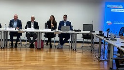 Vier Menschen sitzen an einem Tisch mit Mikrofon