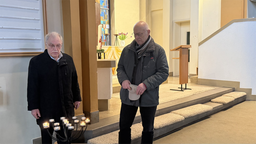 Zwei Personen stehen in der Kirche vor einem Kerzenständer
