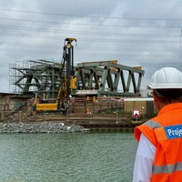 Mann mit Warnweste auf der "Projektleitung DB" seht, betrachtet Großbaustelle.