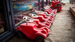 Mehrere rote Bobbycars vor einer Glaswand