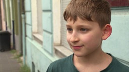 Das Portait eines Jungen, der vor einer Häuserwand draußen steht