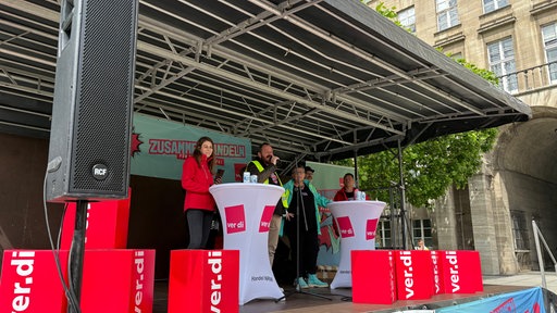 Menschen stehen auf der Bühne und halten eine Rede bei einer Verdi Veranstaltung