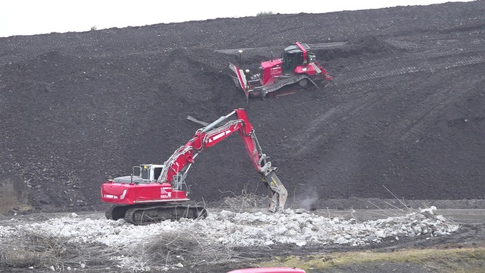 Baustellenfahrzeuge verschieben Erde auf dem Haldenkopf und reißen den Beton des Amphietheaters ein.