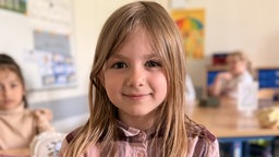 Matilda sitzt in Klassenraum und hat Schüler im Hintergrund. 
