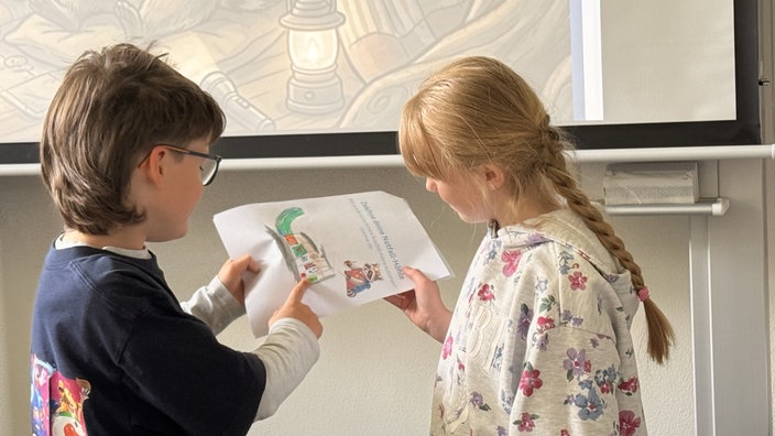 Zwei Kinder blicken auf ein selbstgemaltes Bild mit der Überschrift "Zeichne deine Notfall-Höhle"