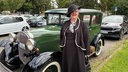 Eine Frau mit schwarzem Hut und Kostüm steht vor ihrem grünen Ford Modell A von 1930.