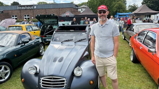 Ein Mann mit roter Kappe präsentiert auf dem Oldtimertreffen in Bottrop seine anthrazit Rennente.
