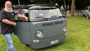 Ein Mann steht neben seinem umgebauten, grauen VW Bulli T2 von 1968.
