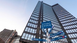 Der hohe Turm des Essener Rathauses von außen, davor ein Wegweiser mit den Partnerstädten von Essen