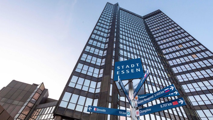 Der hohe Turm des Essener Rathauses von außen, davor ein Wegweiser mit den Partnerstädten von Essen