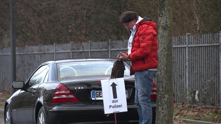 Mann steht mit Auto hinter Polizei-Hinweisschild