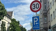 Eine Straße mit Tempo-30-Schild und einem Hinweis auf Parken nur mit Parkschein. 