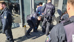 Zwei Polizisten kontrollieren einen Mann, welcher gegen eine Wand am Hauptbanhof gestellt ist.