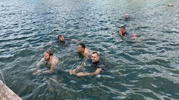 Auf dem Bild sieht man Stahlarbeiter, die im Wasser schwimmen