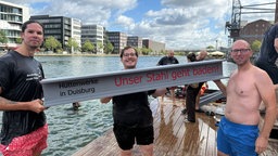 Auf dem Bild sieht man Stahlarbeiter, die ein Schild hochhalten. Auf dem Schild steht "Unser Stahl geht davon"