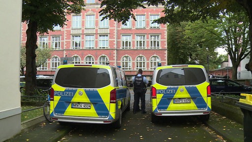 Zwei goße Polizeiautos, zwischen ihnen steht ein Polizist mit dem Rücken zur Kamera. 