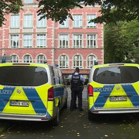 Zwei goße Polizeiautos, zwischen ihnen steht ein Polizist mit dem Rücken zur Kamera. 